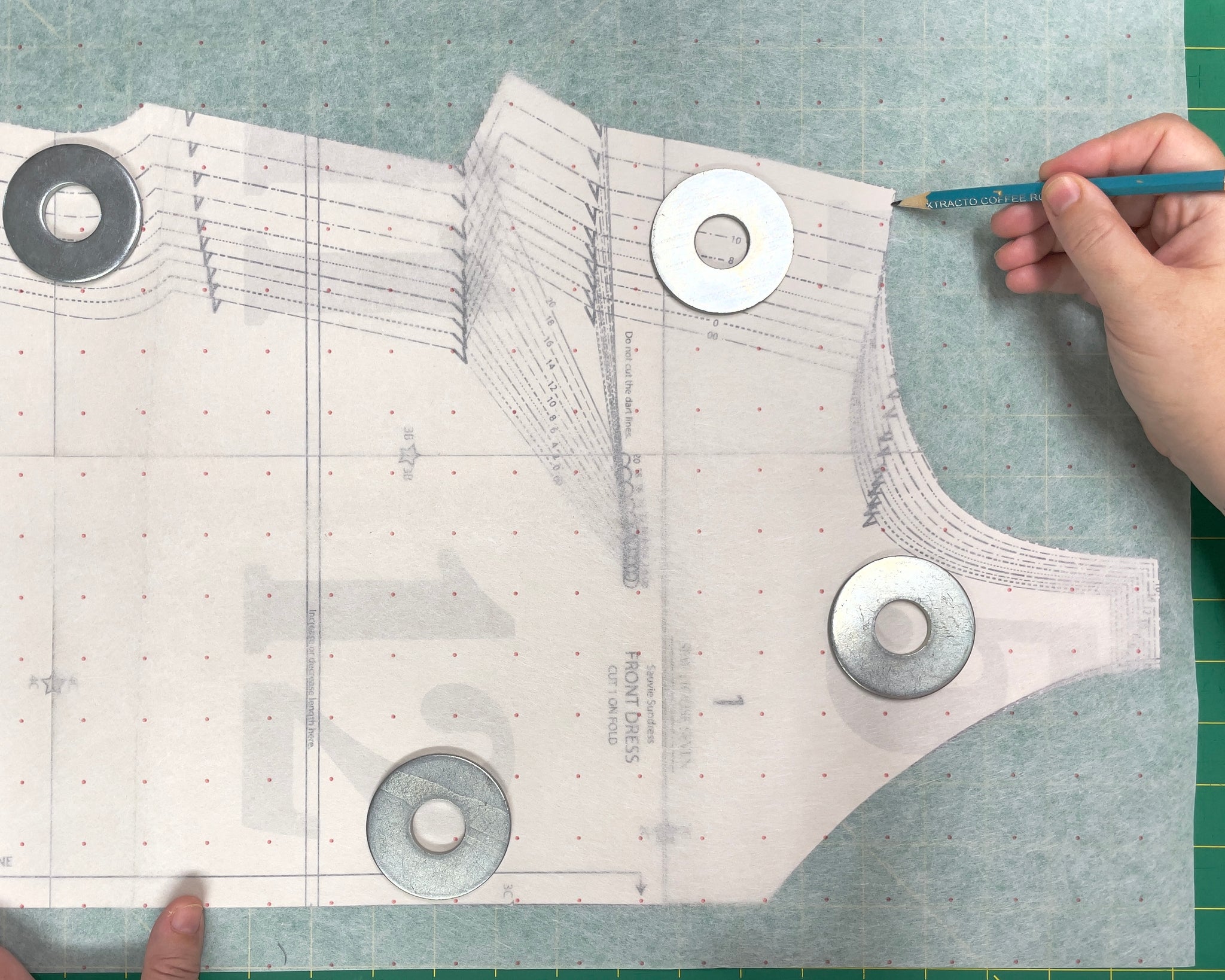 The Front Dress pattern piece from the Sauvie Sundress, with tracing paper laid on top. A hand is tracing the pattern with a pencil