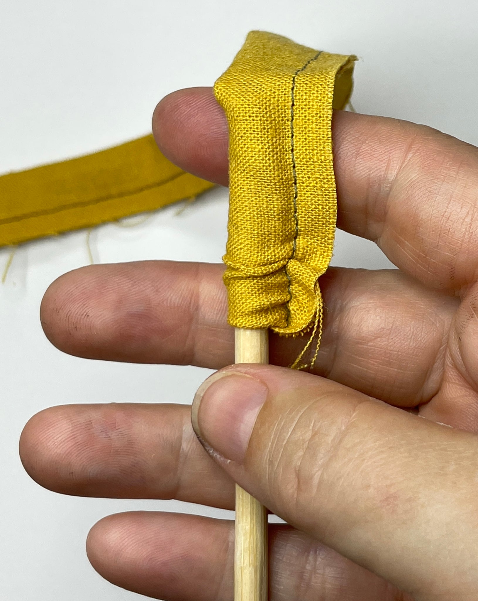 Turning the yellow waist tie right side out on a chopstick