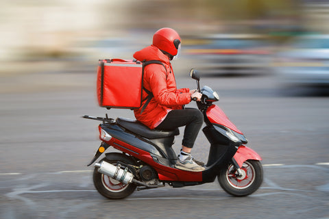 A man on a red scooter is on the way to deliver items.