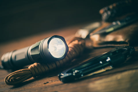 A lit flashlight lies on a table over a tied cord.