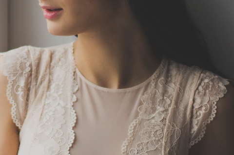 Person wearing top with lace fabric details in front of gray background.