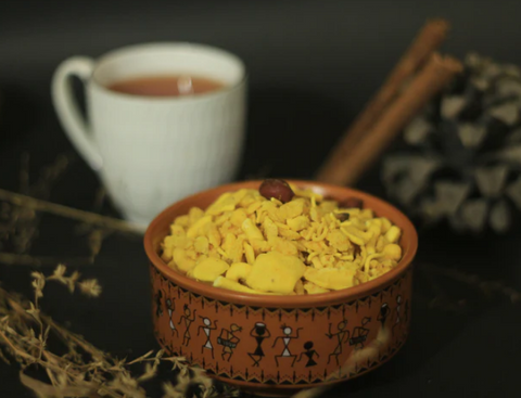 A red bowl of Khatta Meetha mix with a tea cup in background