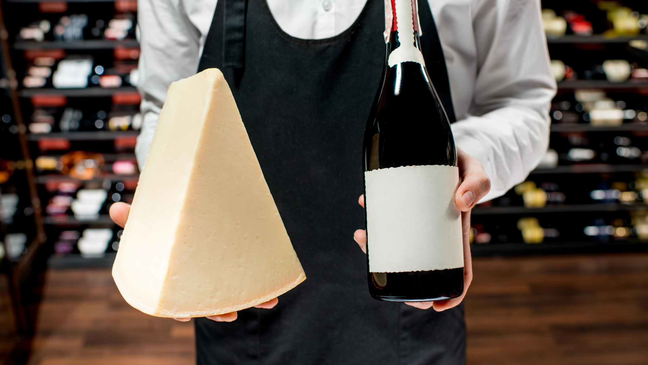 a person holding a bottle of wine and a piece of cheese