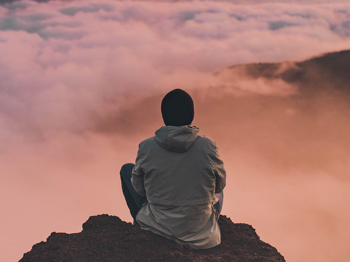 A person meditating outside on the rocks with a gorgeous sunset in front of them.