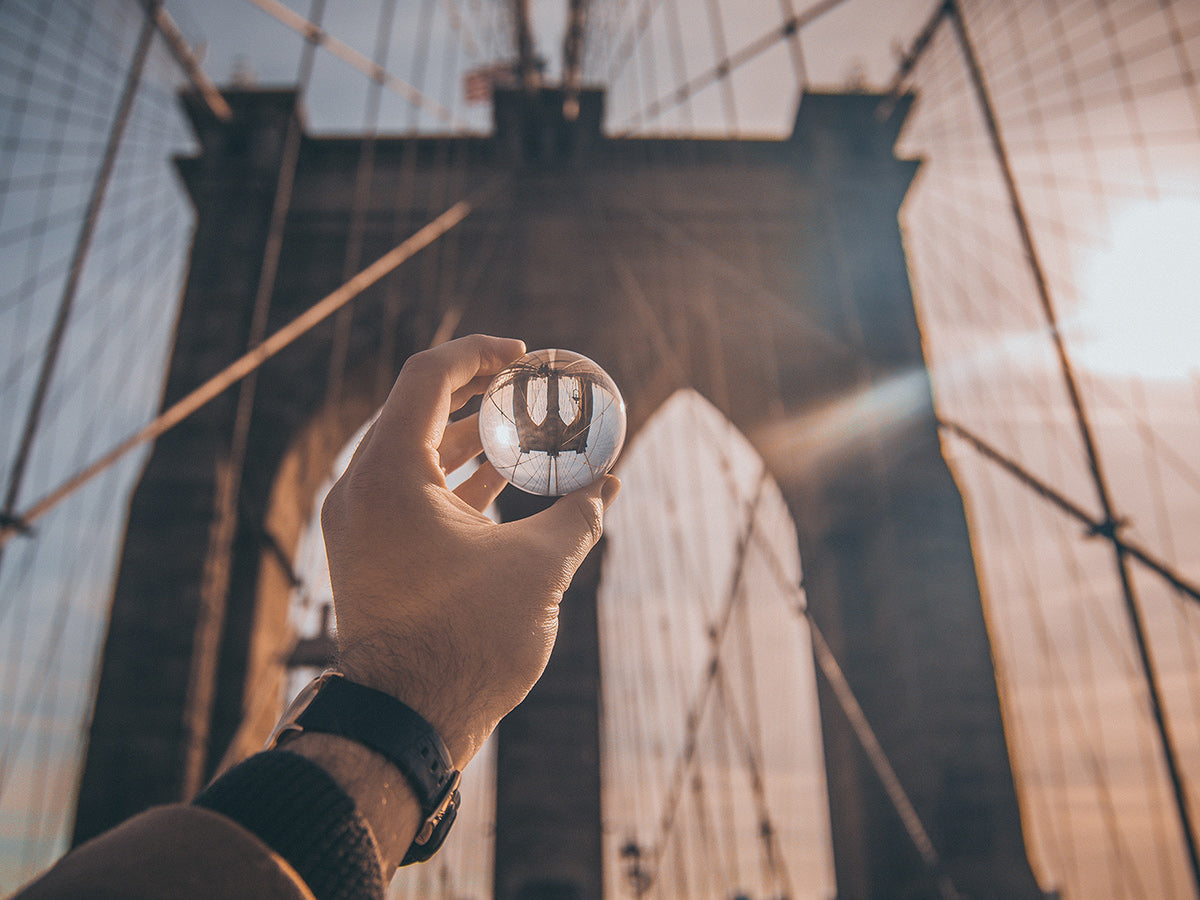 A person holding a glass ball up to the Brooklyn Bridge, changing it’s perspective.