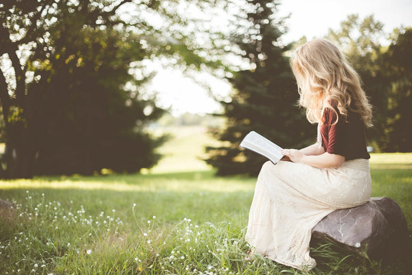 Femme dans un champ qui lie un livre avec une robe bohème