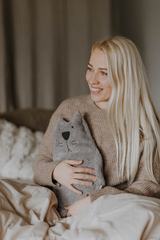 young woman holding hot water bottle with grey cotton cover cat