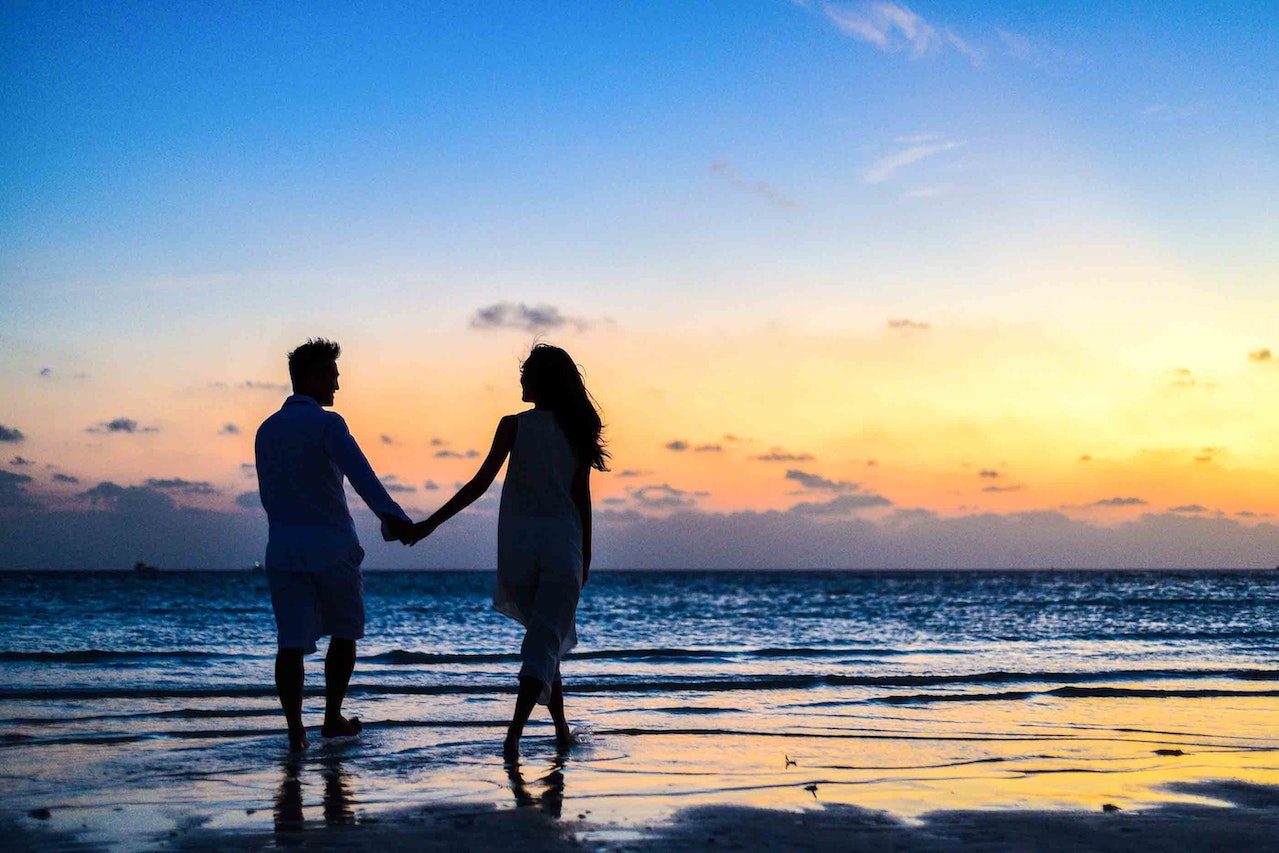 Casal romântico de mãos dadas na praia ao pôr do sol