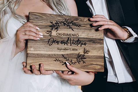pareja sosteniendo una tabla de cortar grabada con la fecha y los nombres de la boda