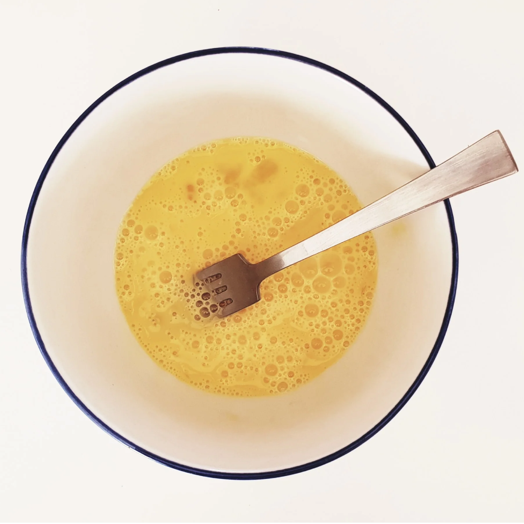 A bowl of beaten eggs with a fork in it.