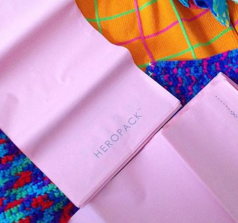 A close up of two pink compostable Hero Pack mailers with an orange and blue knit jumper in the background about to be packaged.