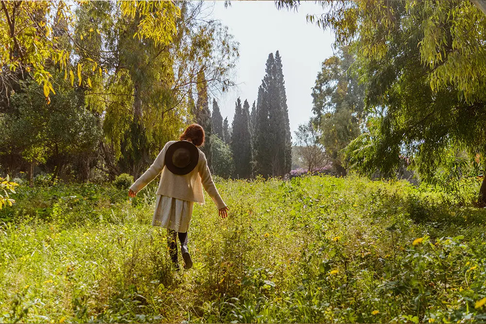 femme de dos qui se promenade dans la foret avec un chapeau sur le dos bain de foret appel de la nature pour le stress