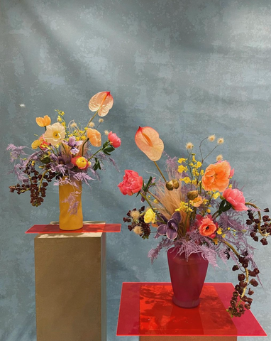 Pedestals hold artfully arranged colorful florals on a blue background