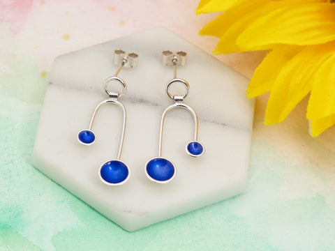 Silver earrings with blue enamel, shown on a tile with a sunflower