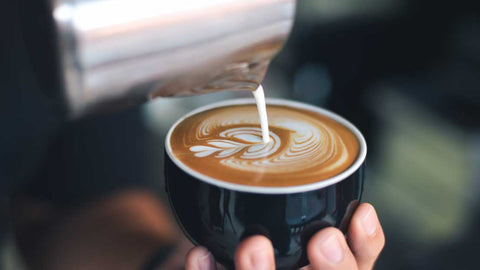 Milch wird in Kaffee gegossen, um Latte Art zuzubereiten