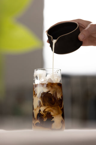 pouring milk into a cup of iced coffee