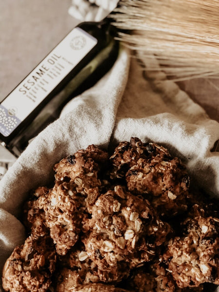 A pile of delicious looking oatmeal raisin cookies next to a bottle of our Organic Sesame Seed Oil from Pure Indian Foods