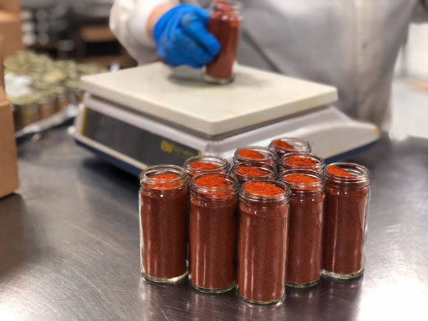 Jars of kashmiri red chili powder being weighed by hand.