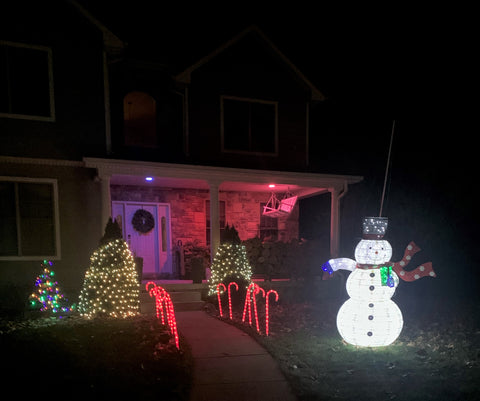 Front yard of a house with holiday lights, bright snowman, and pink and purple lit porch