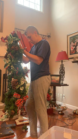 Abram hanging lights on a Christmas tree in his family's living room