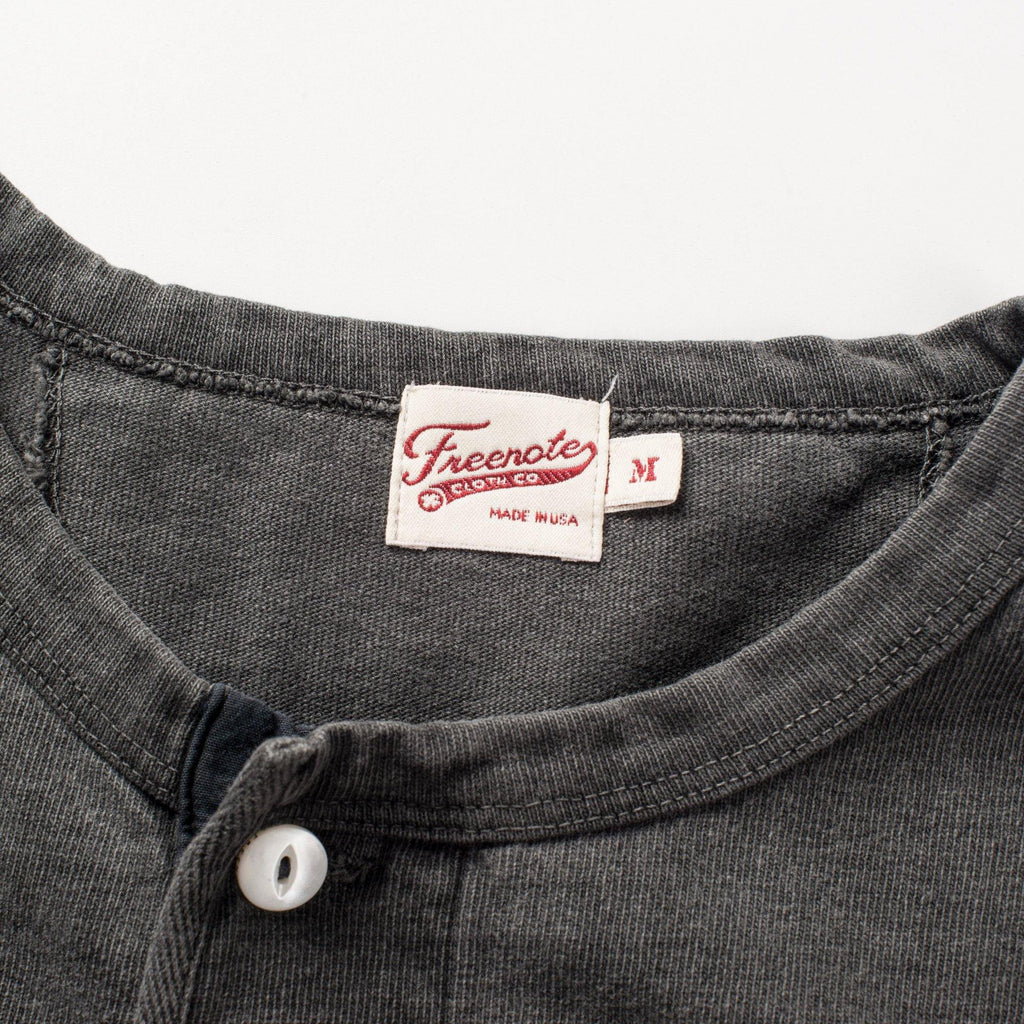 The Freenote Cloth 13 Ounce Henley Long Sleeve Shirt in Midnight. The shirt has three white buttons leading up to the collar that are all closed.  The photo is zoomed in on the freenote cloth co logo and medium size label 