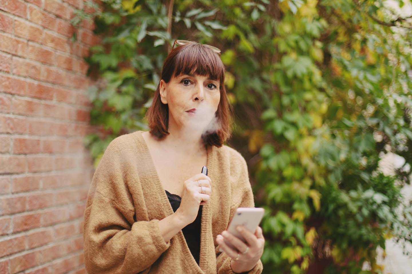A woman in brown sweater holding a mobile phone while vaping