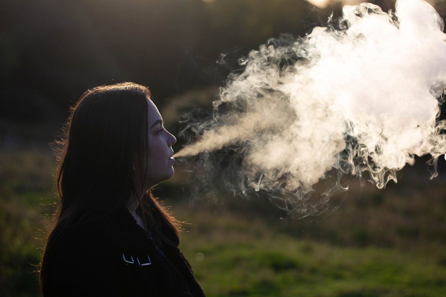 woman standing in the grass blowing a vape cloud