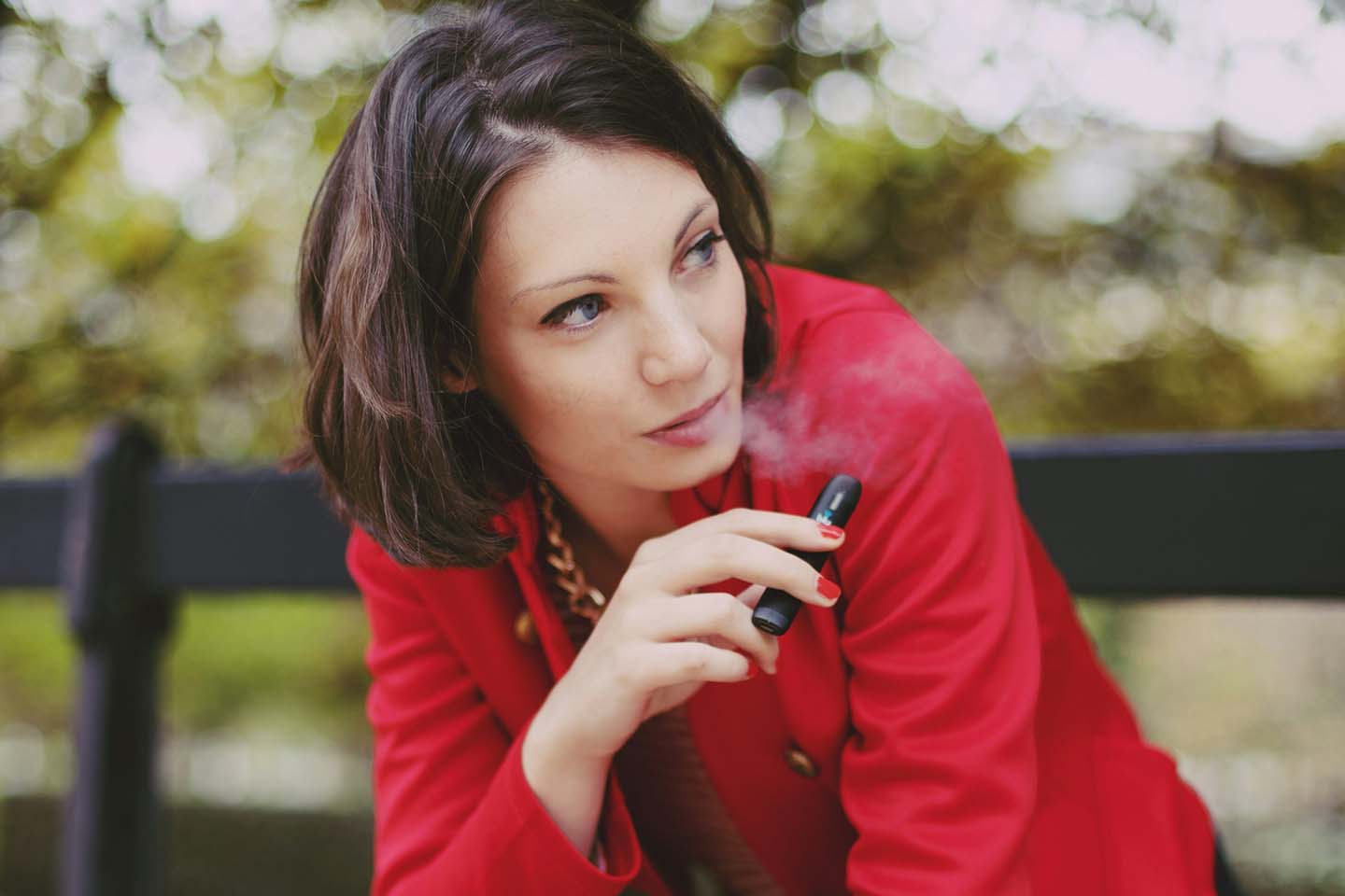 a woman in red sitting on a park bench while vaping