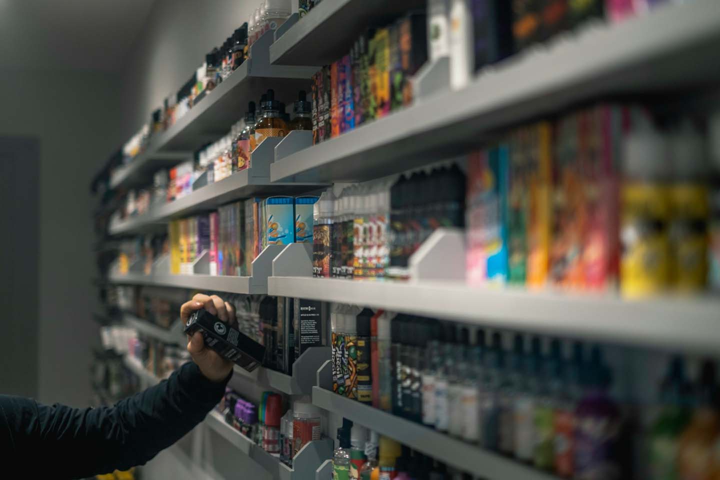 person selecting a packaged vape from a shelf filled with various vapes