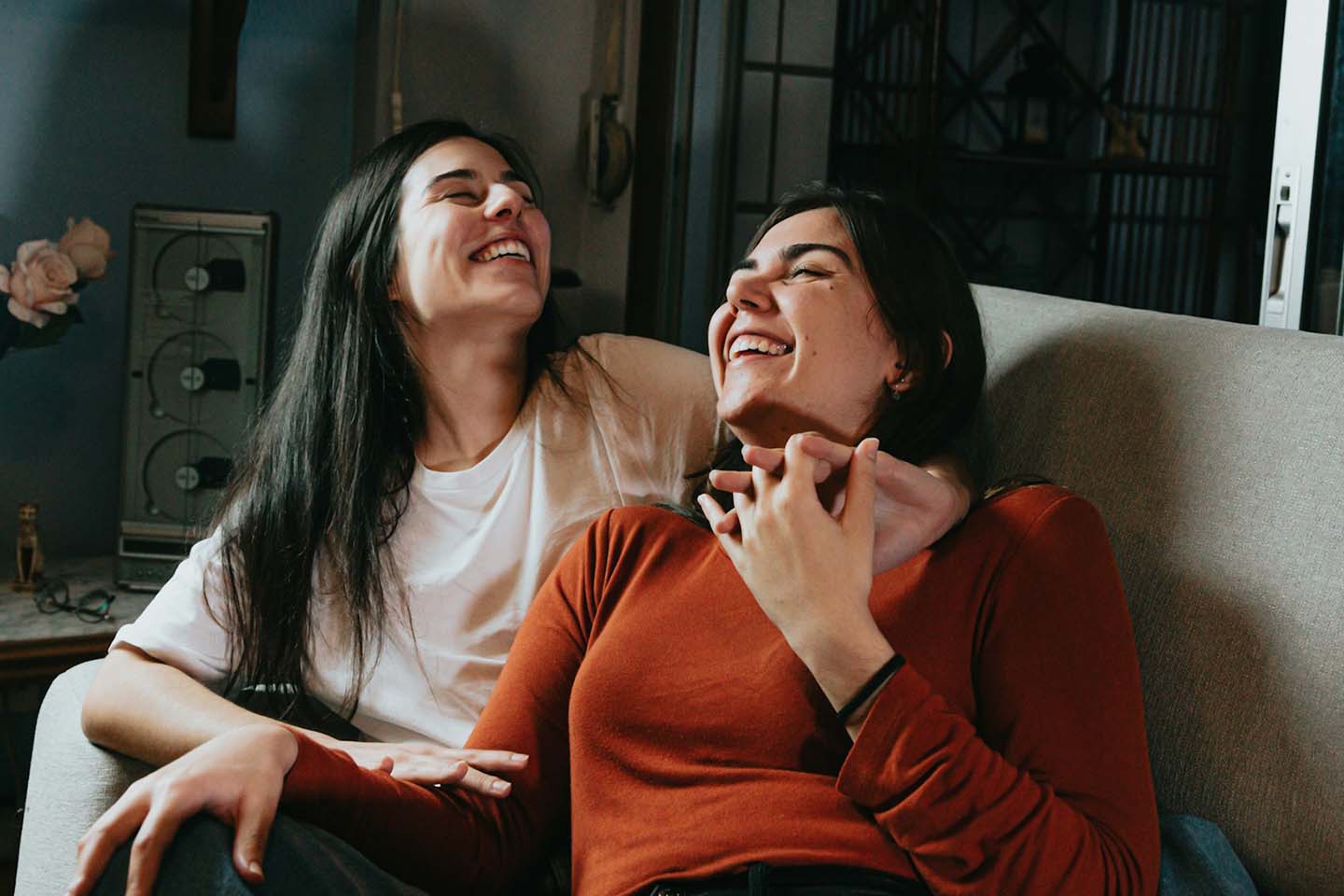 two women sitting on a sofa while having fun laughing