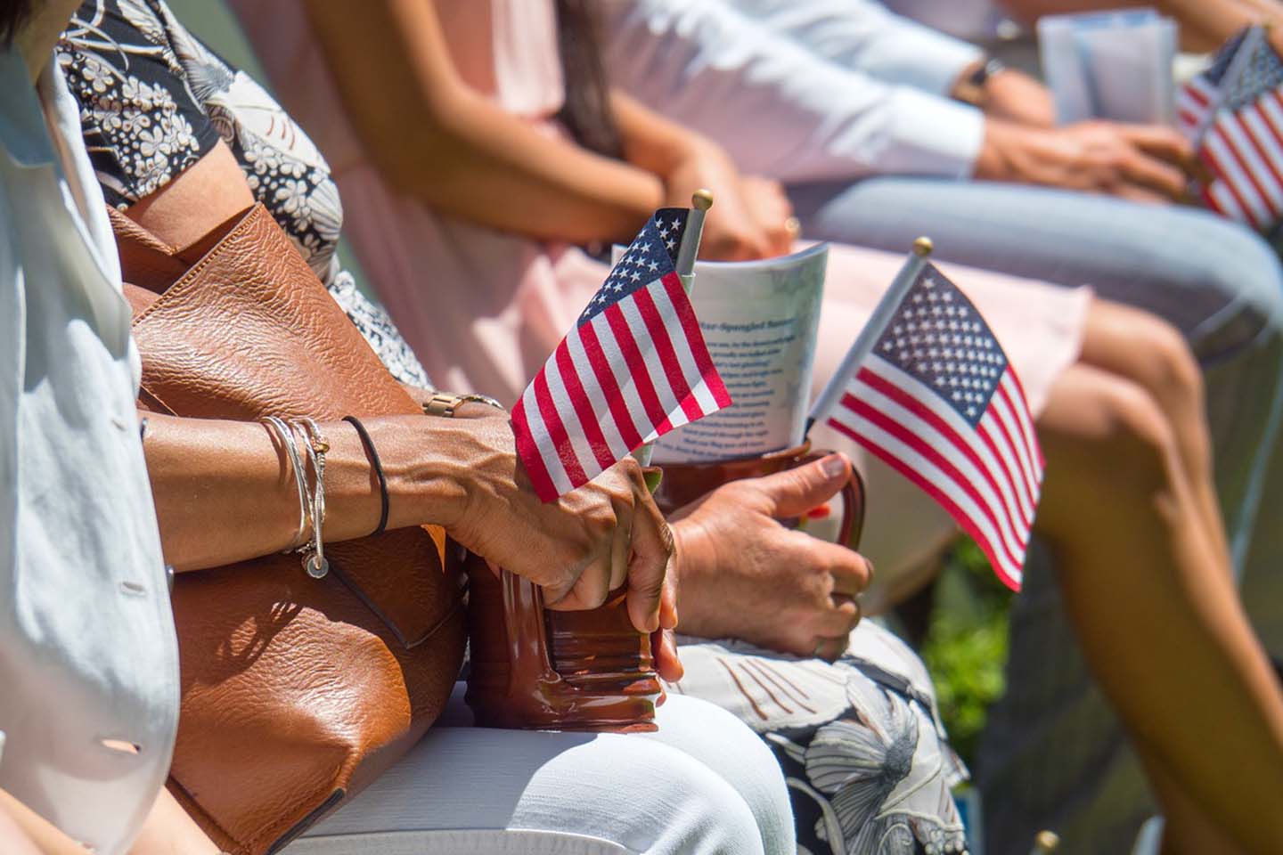 Four people sitting at a parade, each person holding one small American flag.