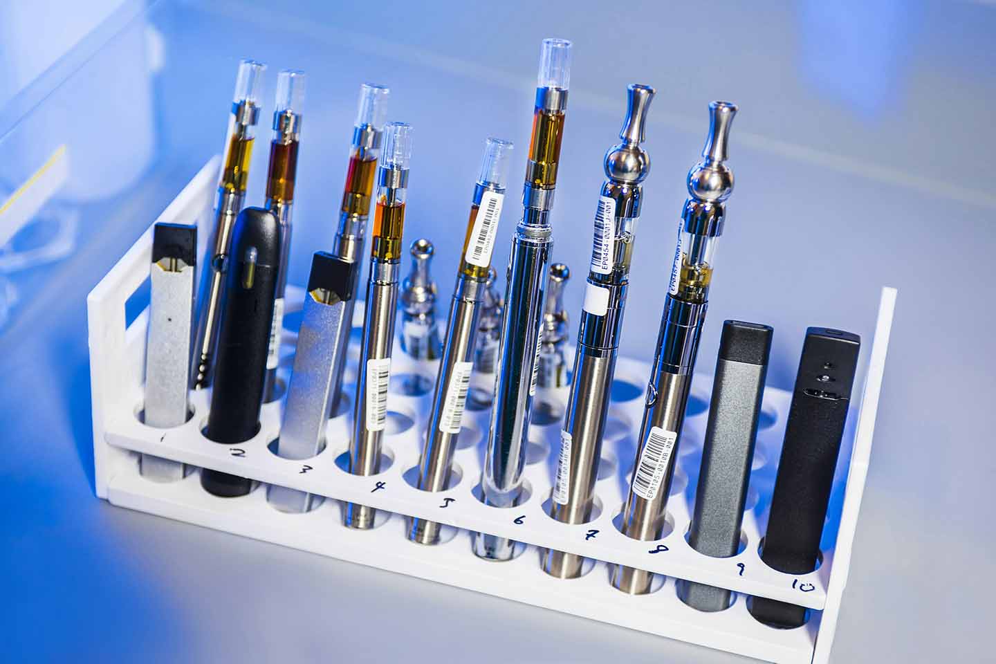 Several disposable vapes in a test tube stand on a desk.