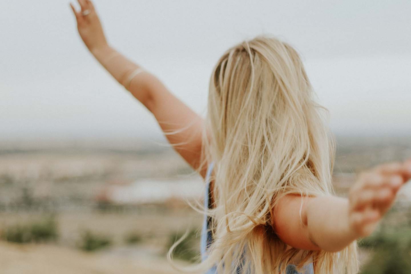 blonde woman outside with outstretched arms