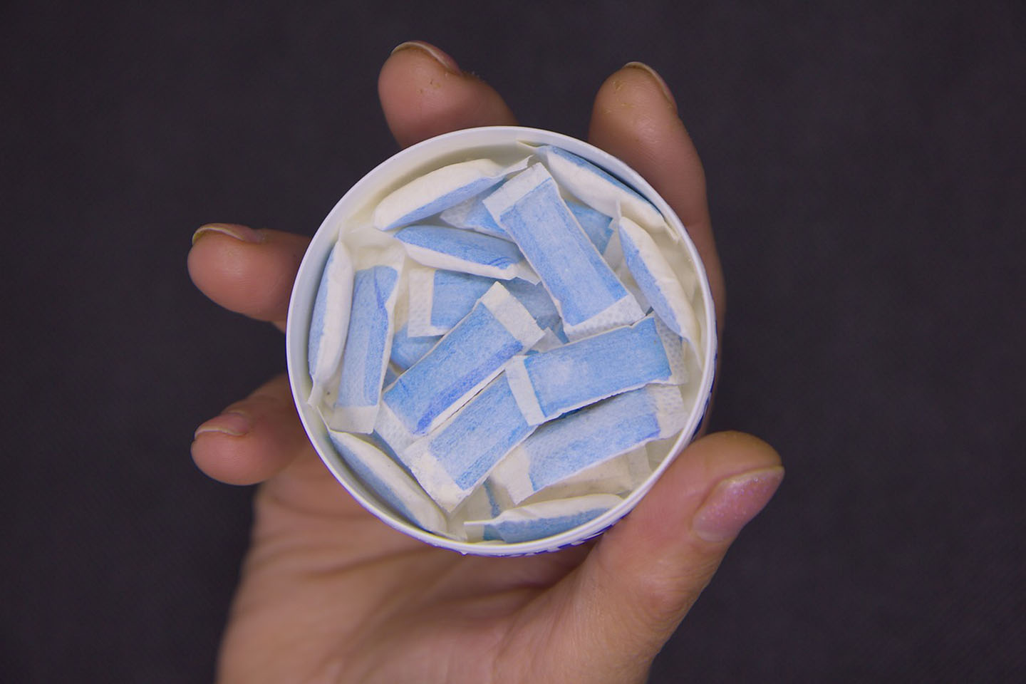 Person holding tin of blue and white nicotine pouches