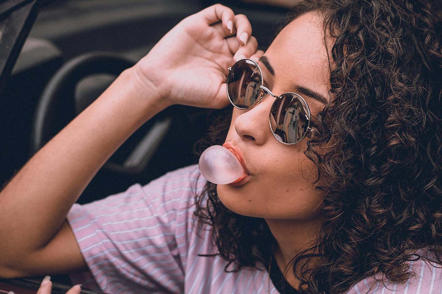 a woman with sunglasses blowing a bubblegum bubble in a car