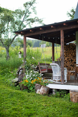 A corner of a porch at Stitchdown Farm with a porch swing and a large stack of firewood. 