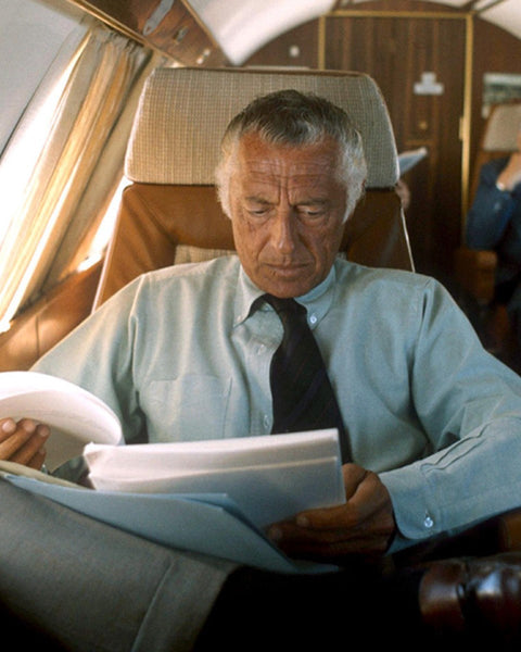 Gianni Agnelli wearing a light blue OCBD shirt with while reading a paper in an airplane