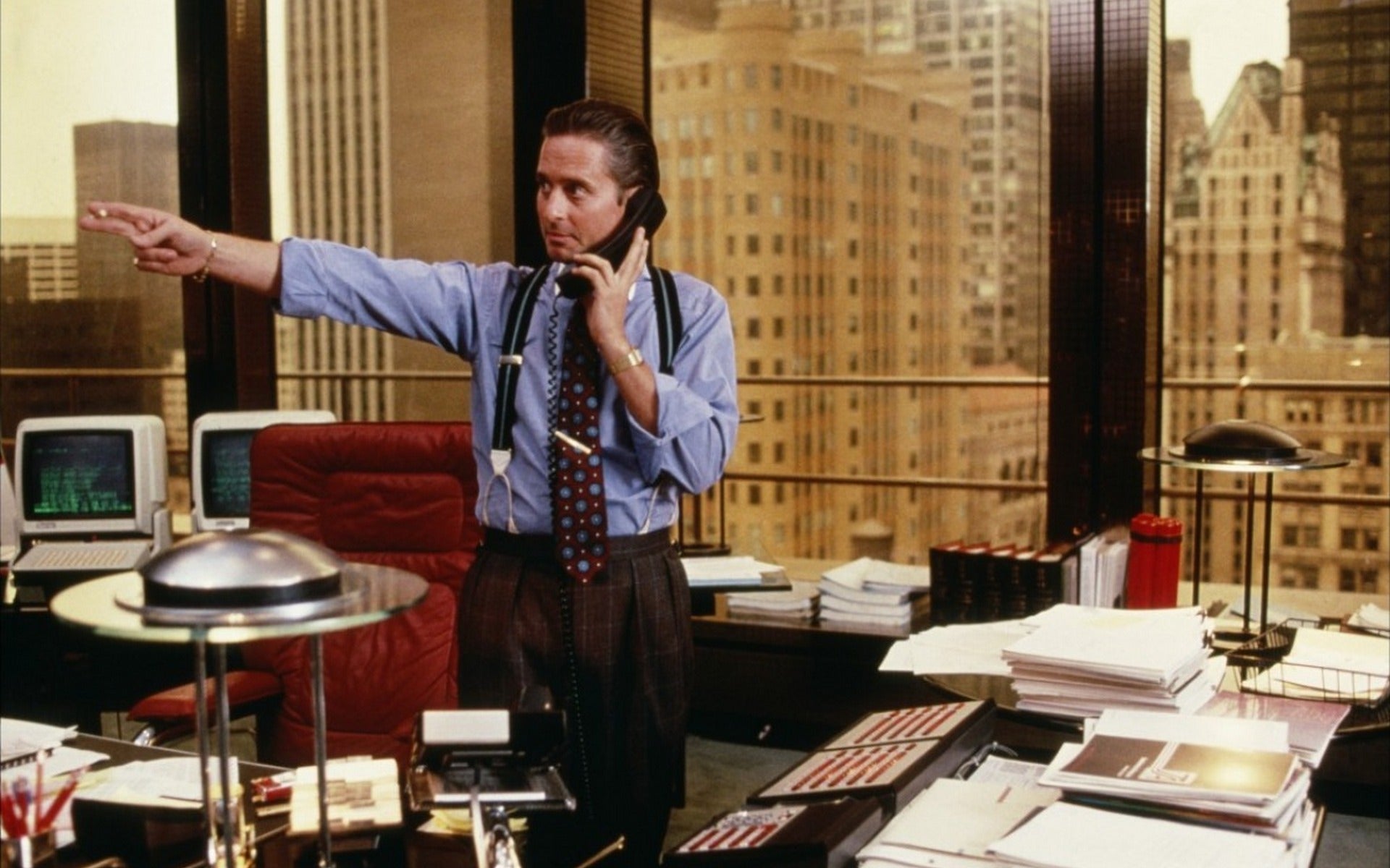 Michael Douglas as Gordon Gekko wearing a blue end-on-end contrast collar shirt with eton striped suspenders in Wall Street 