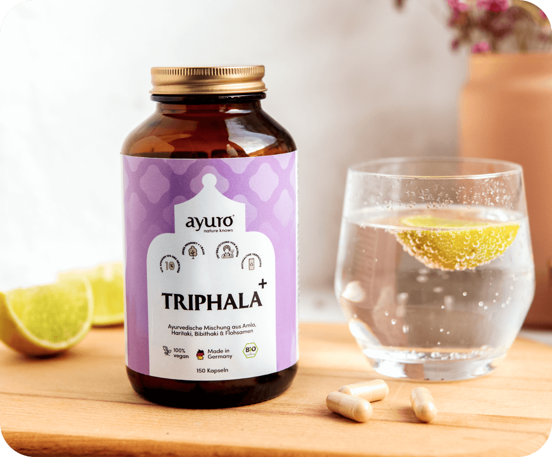 Triphala Produkt Kapseln auf einem Brett mit Zitrone und einem Glas Wasser