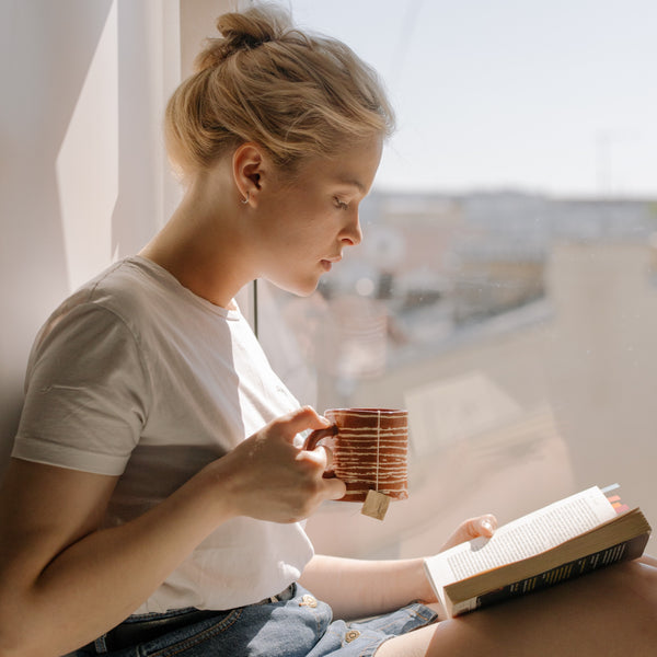 girl reading a book while she's drinking a cup of Tearapy BoosTea tea