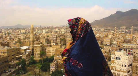 Mujer con velo en una montaña frente a ciudad en Yemen. Imagen de Qima Coffee para la presentación de la nueva población madre de café Yemenia