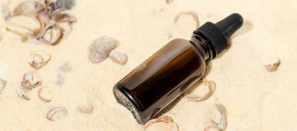 essential oil bottle on sandy beach with shells