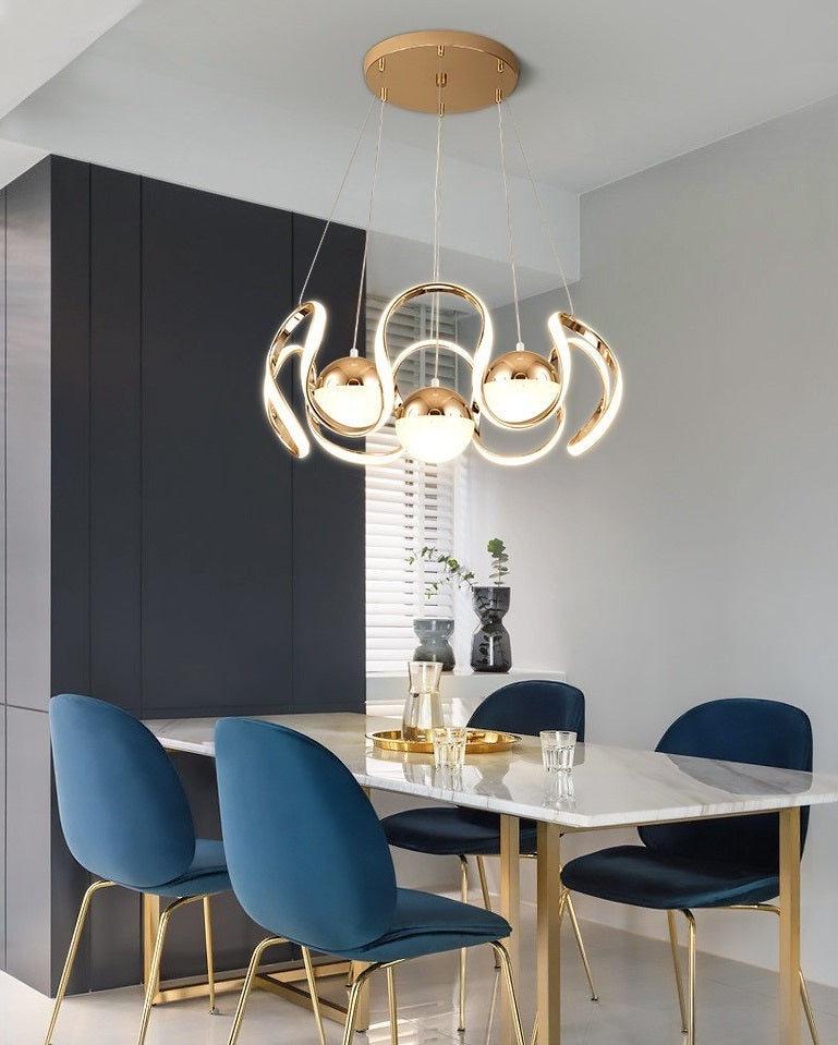 A minimalist modern dining room with blue chairs and a gold Ohm Pendant Light, exuding a Nordic vibe.