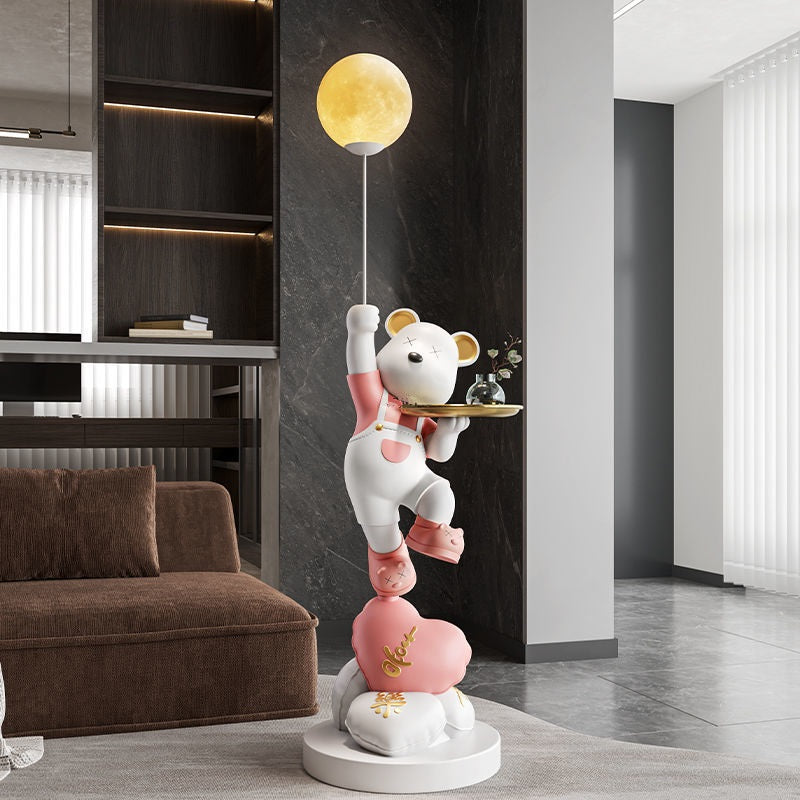 A whimsical floor lamp featuring stacked bears in different colors reaching for a glowing moon, placed in a modern living room to create a welcoming atmosphere.