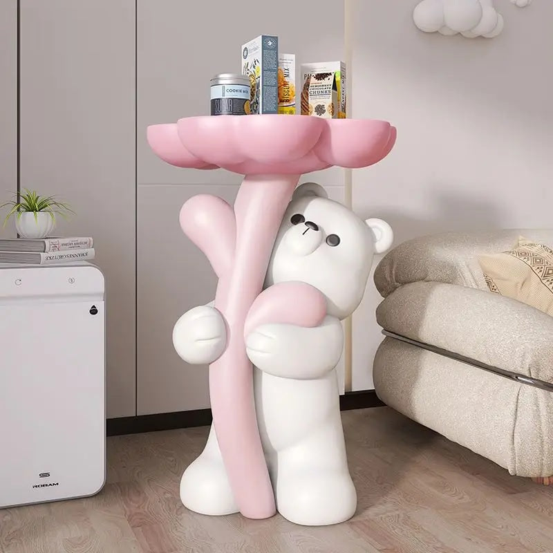 A decorative piece featuring a floral bear figurine holding a pink, flower-shaped platform used as a side table, placed in a cozy room corner.