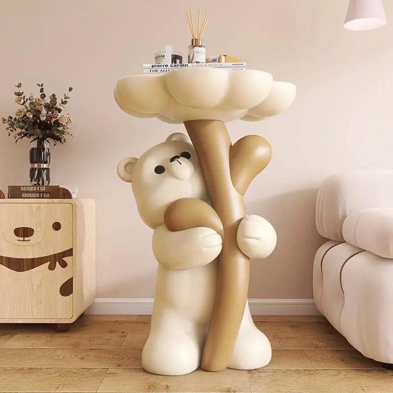 A whimsical side table in the shape of a cartoon bear holding up a flower shaped tabletop, next to a wooden cabinet with floral decor.