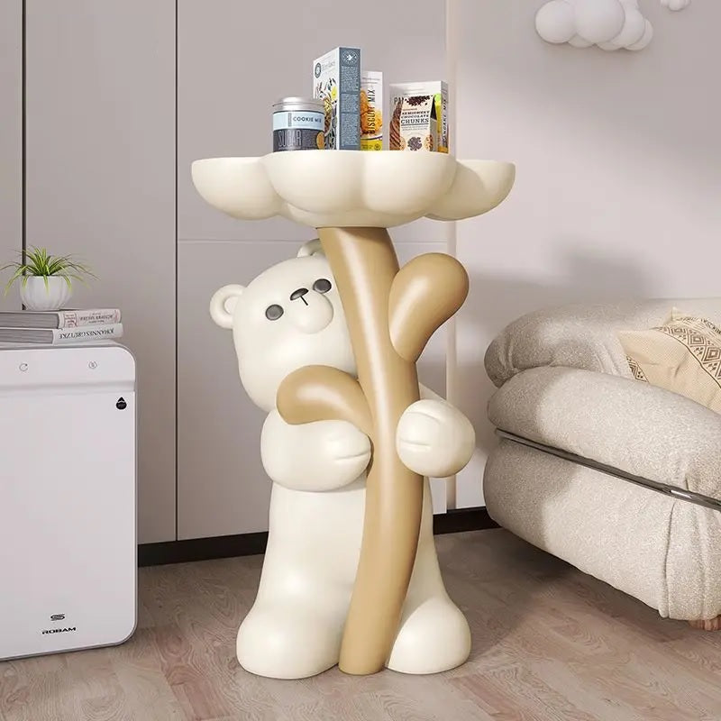 A decorative piece featuring a floral bear figurine holding a pink, flower-shaped platform used as a side table, placed in a cozy room corner.