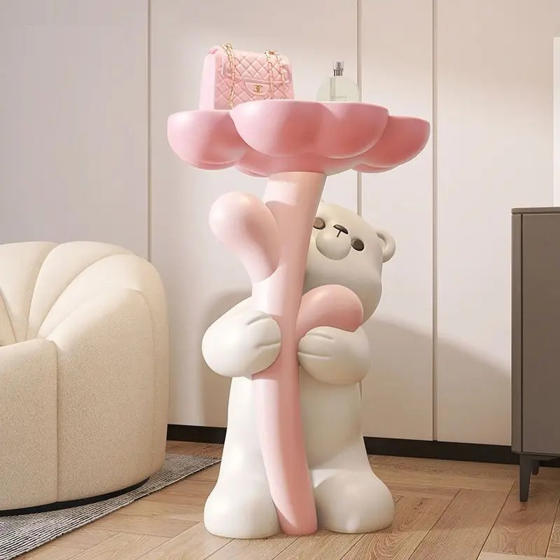 A decorative piece featuring a floral bear figurine holding a pink, flower-shaped platform used as a side table, placed in a cozy room corner.