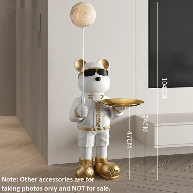 A decorative Bear Statue Night Light of a cartoon-style bear dressed in white and gold, holding a tray and a spherical lamp that emits a soothing glow, stands in a modern room. 