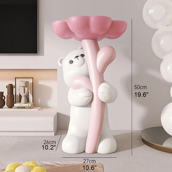 A decorative floral bear-shaped side table in pink and white, holding a balloon, placed in a room beside a wall with balloons.